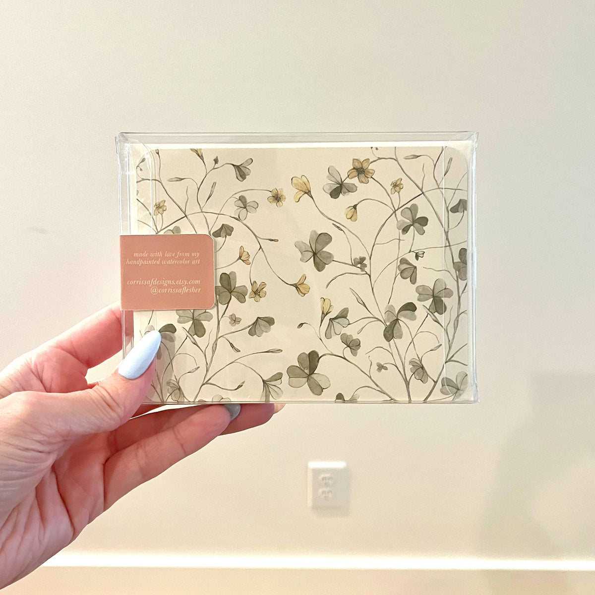 Cream envelope with botanical line floral pattern in a clear plastic sleeve, hand holding