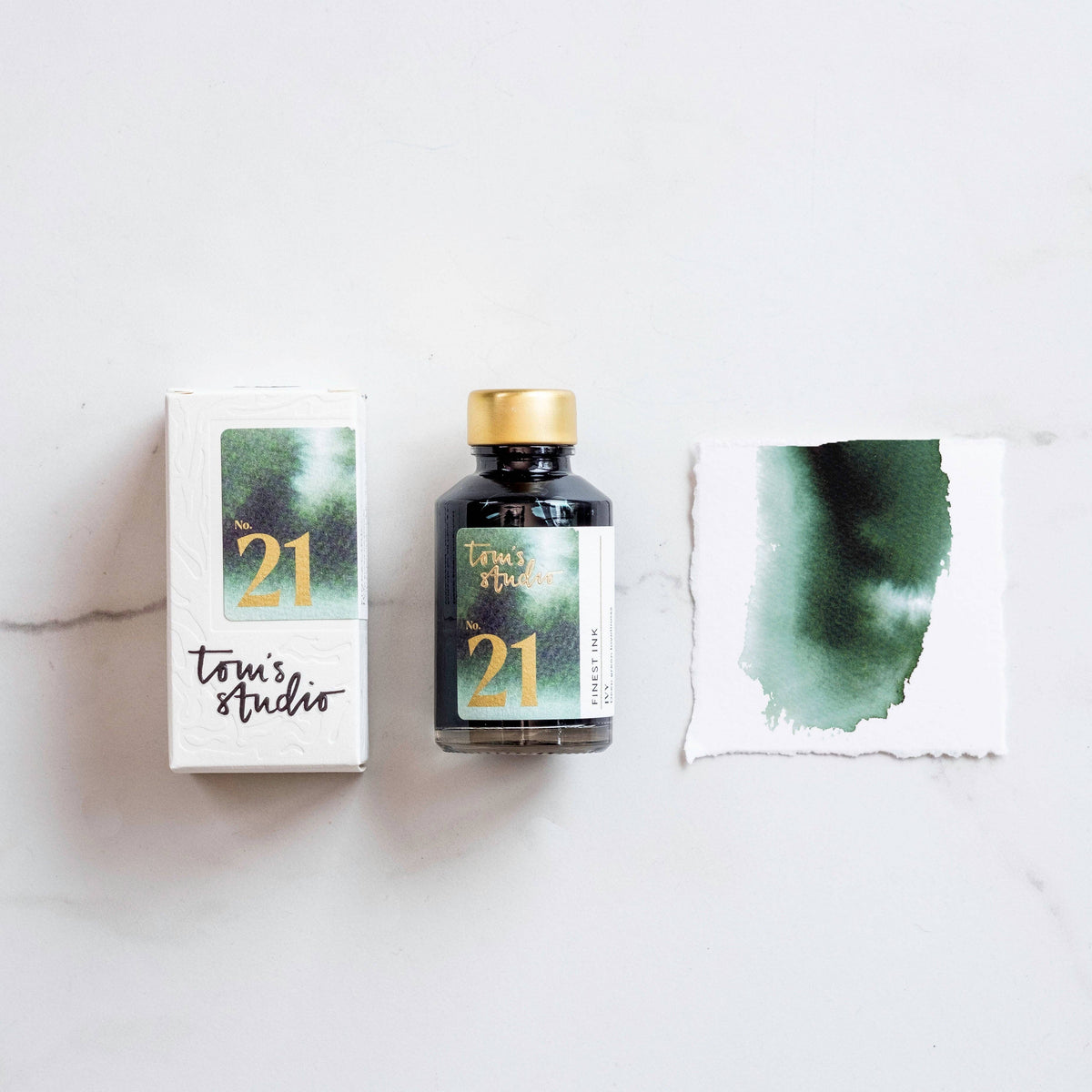 Fountain pen ink bottle with gold cap, box, and green ink swatch