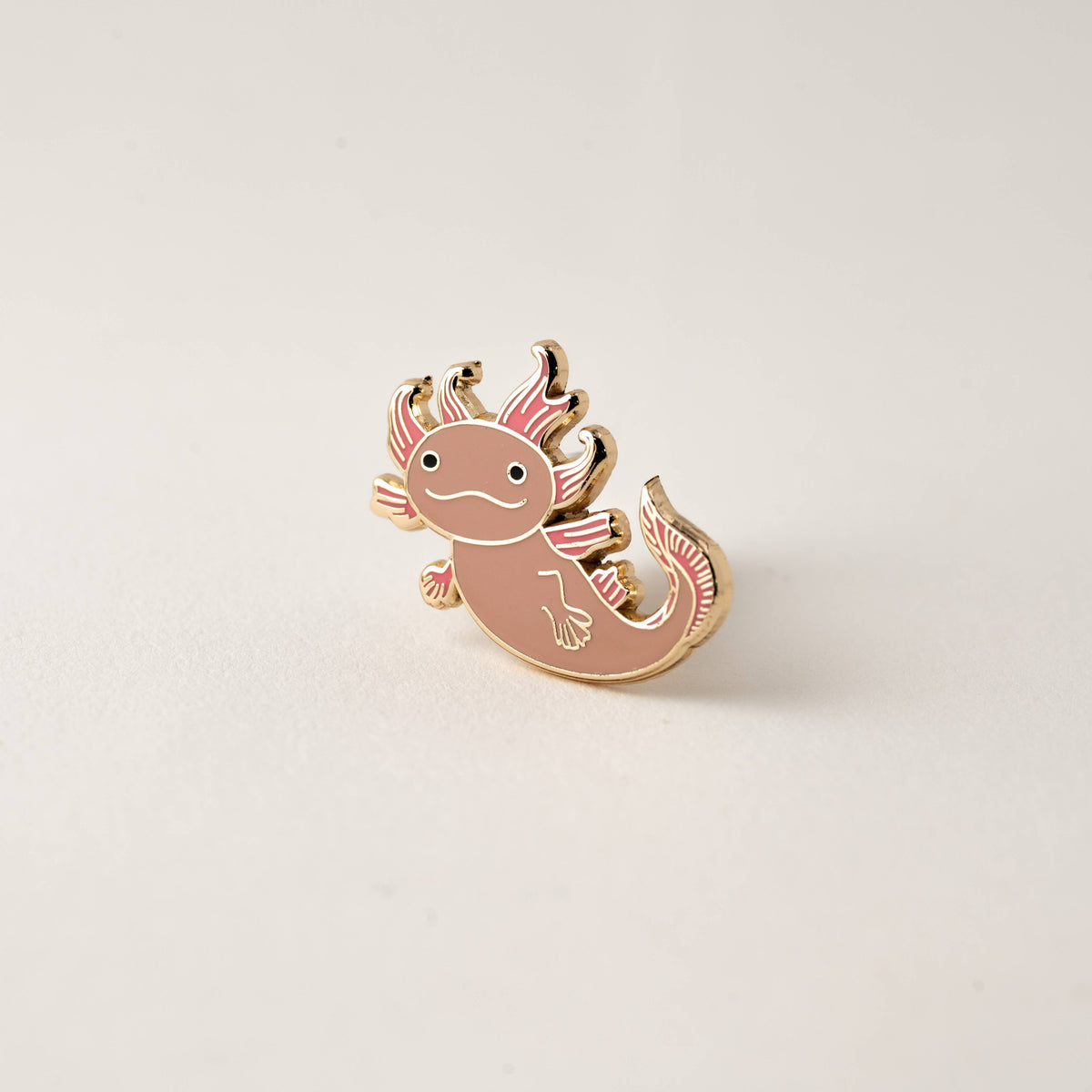 Pink axolotl enamel lapel pin with gold border, smiling face and open fins