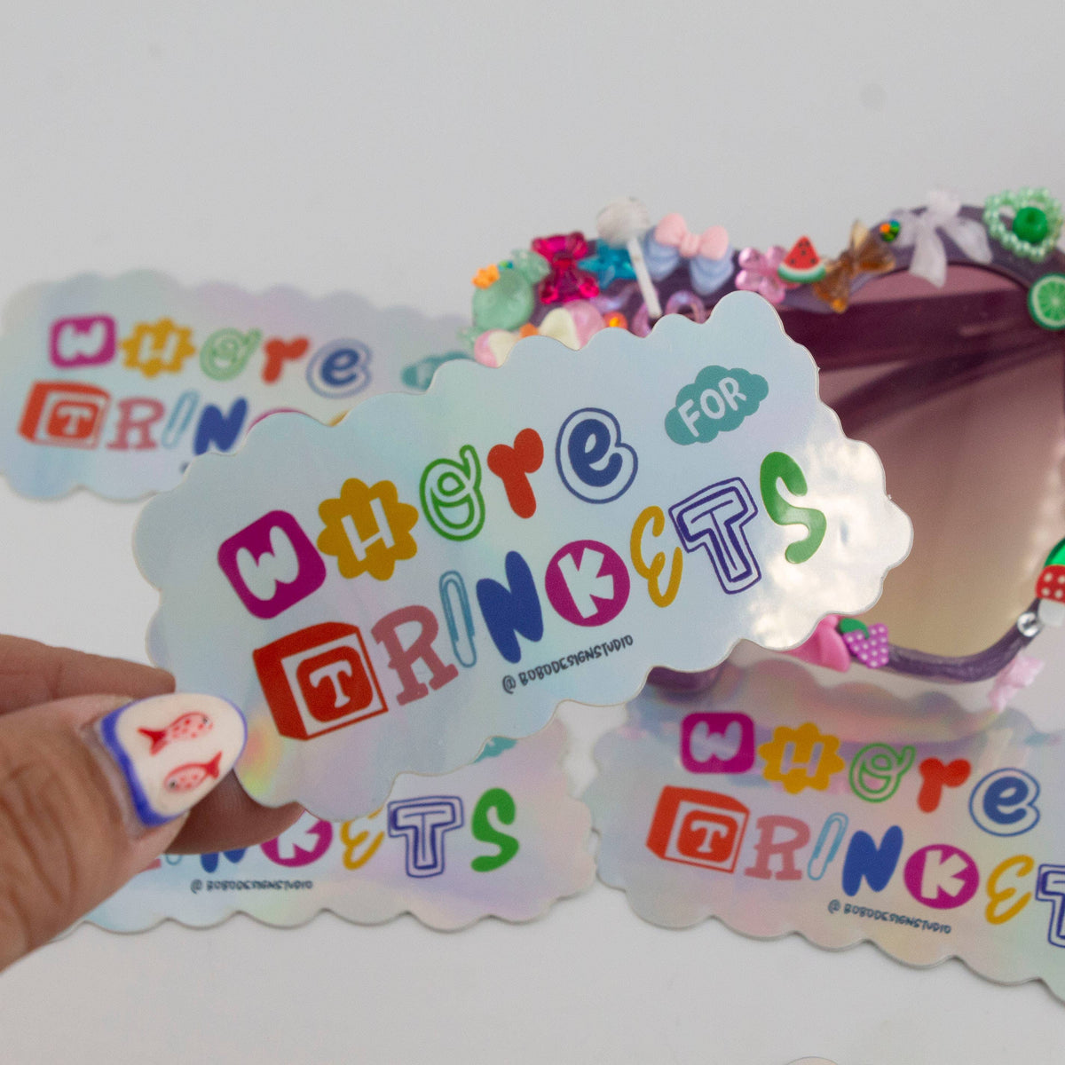 Holographic vinyl sticker with 'Whore for Trinkets' lettering and cloud outline, held
