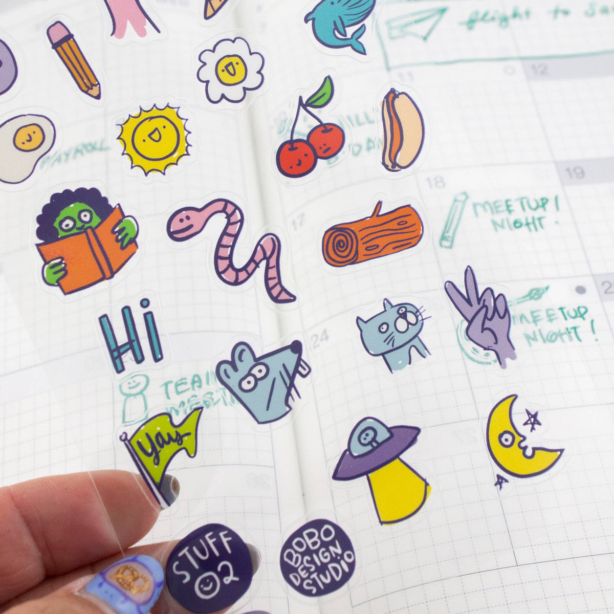 Clear sticker sheet in hand with applied stickers, including “STUFF 02” and “MEETUP NIGHT”