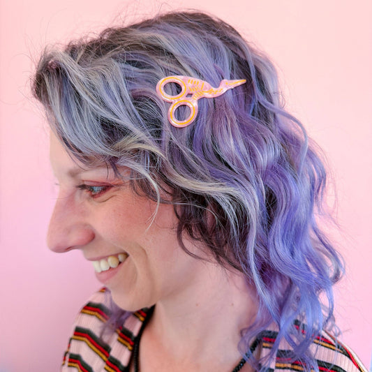 Pink and orange scissors-style hair clip clipped to wavy blue hair