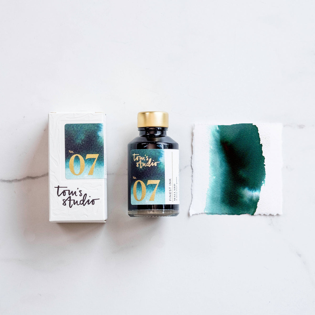 Fountain pen ink bottle with cap, box, and teal-green ink swatch.