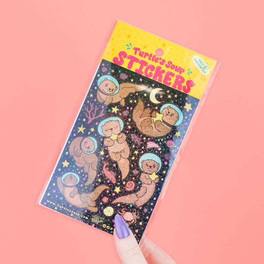 Space galaxy glitter sticker sheet, angled view with otter astronauts and sparkles
