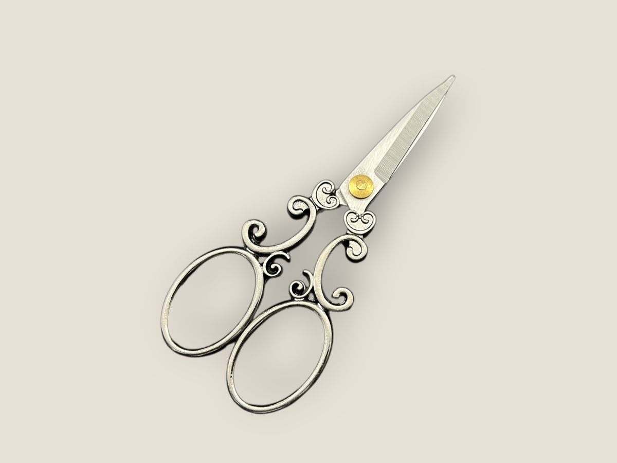 Arabesque scissors close-up with silver blades and black scrollwork, featuring three oval loops