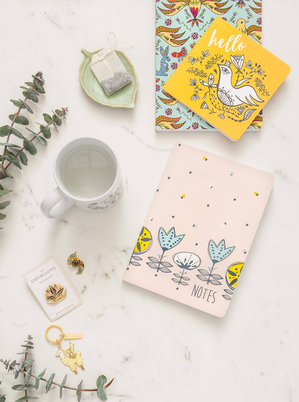 Floral bird enamel pin shown beside its backing card and a matching bird keychain.