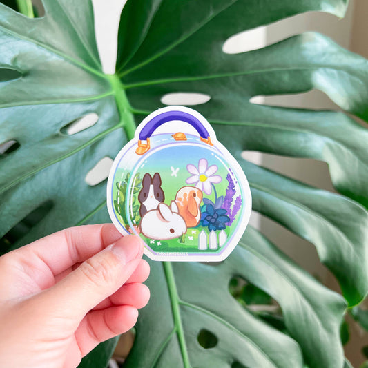 Transparent vinyl sticker held in hand, bunny meadow pouch with rabbit and orange bunny