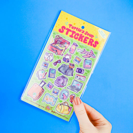 Hand holding a travel sticker sheet with suitcase, camera, passport, and diary icons