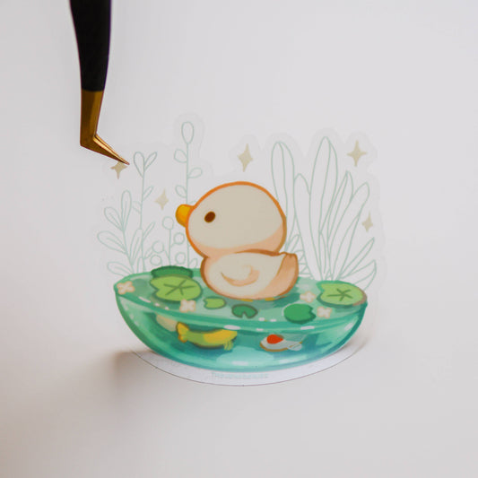 Transparent vinyl sticker illustration of orange-and-white creature in teal pond with plants