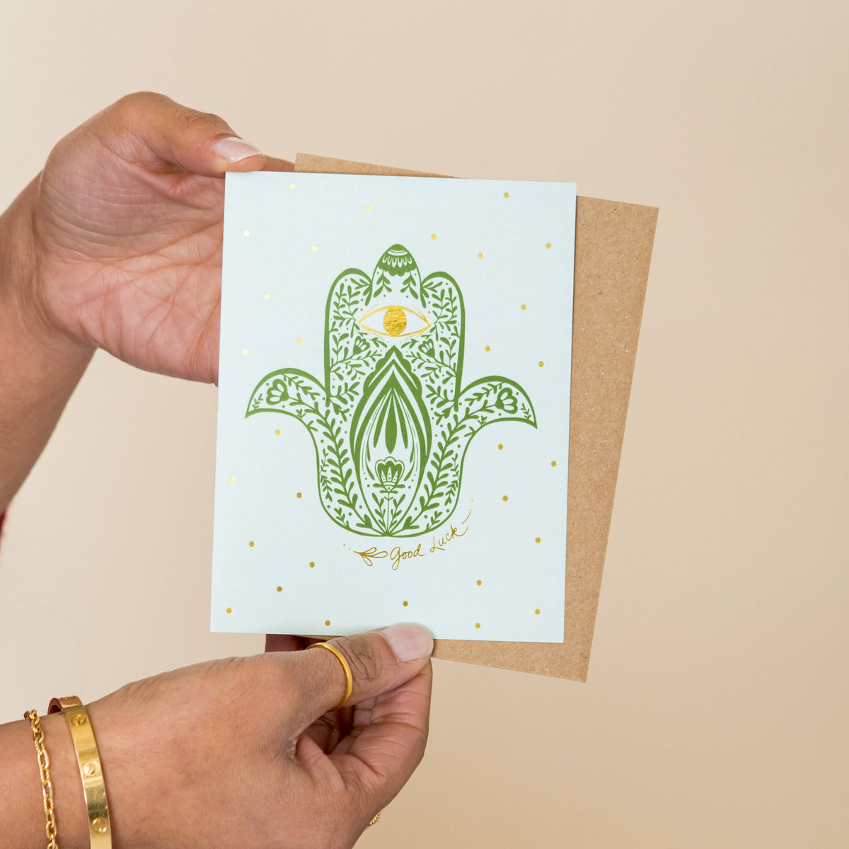 Greeting card featuring a green hamsa hand and gold foil details, shown with its kraft envelope
