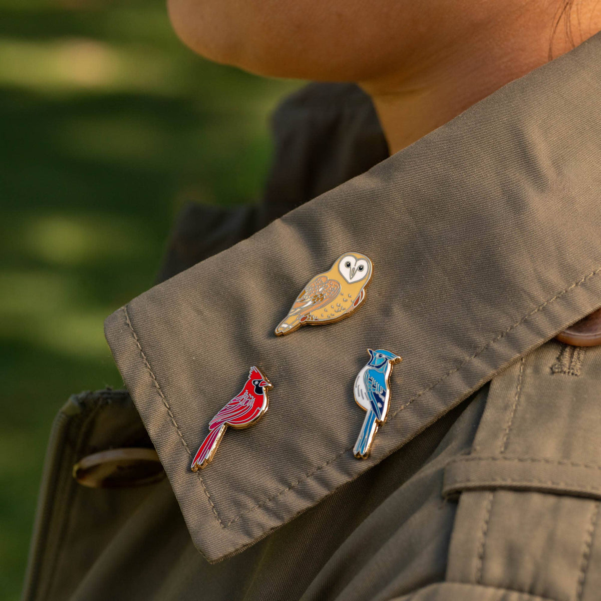 Red cardinal enamel pin on brown jacket with other bird pins