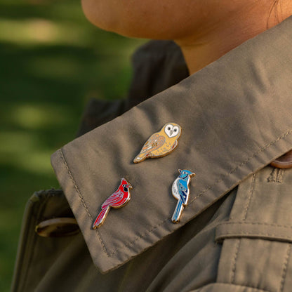 Red cardinal enamel pin on brown jacket with other bird pins