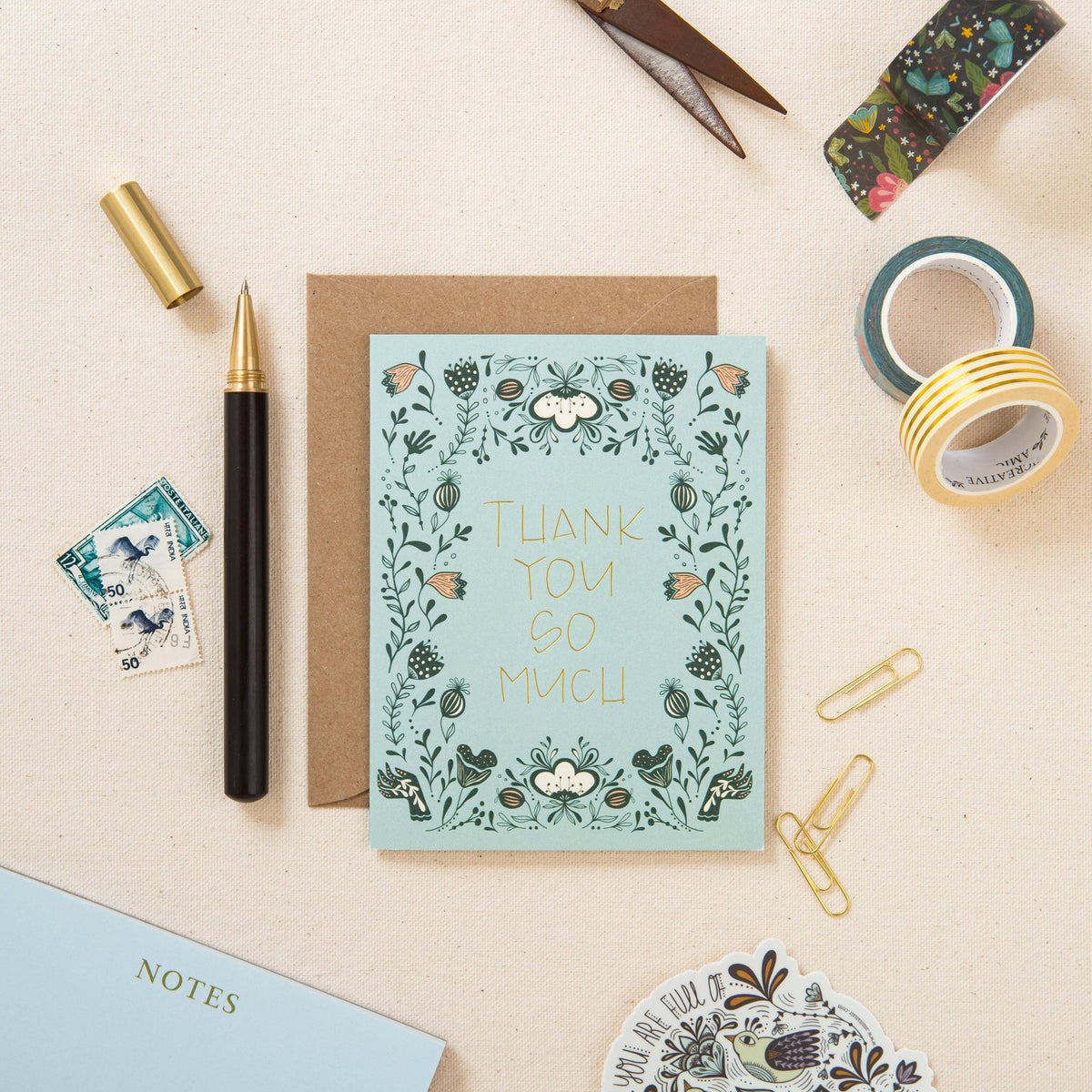 Thank you greeting card with gold foil lettering and floral border, shown with kraft envelope