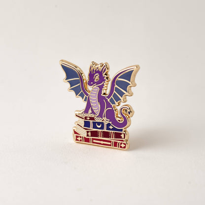 Purple winged dragon book enamel pin with gold outline and stacked books