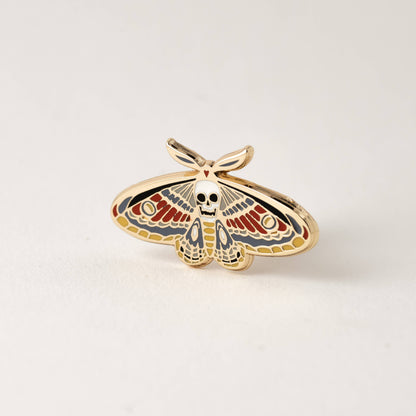 Enamel moth skull pin with colorful wings and gold-tone border