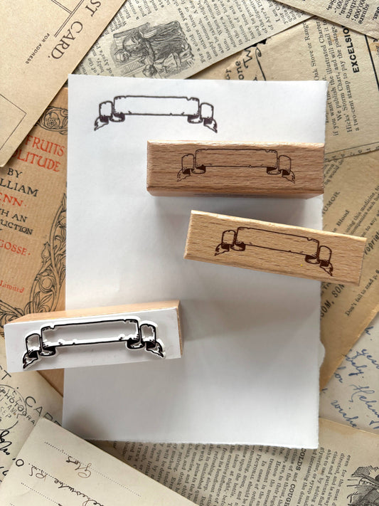 Rubber scroll banner stamp on wooden block with black ink-ready outline, close-up