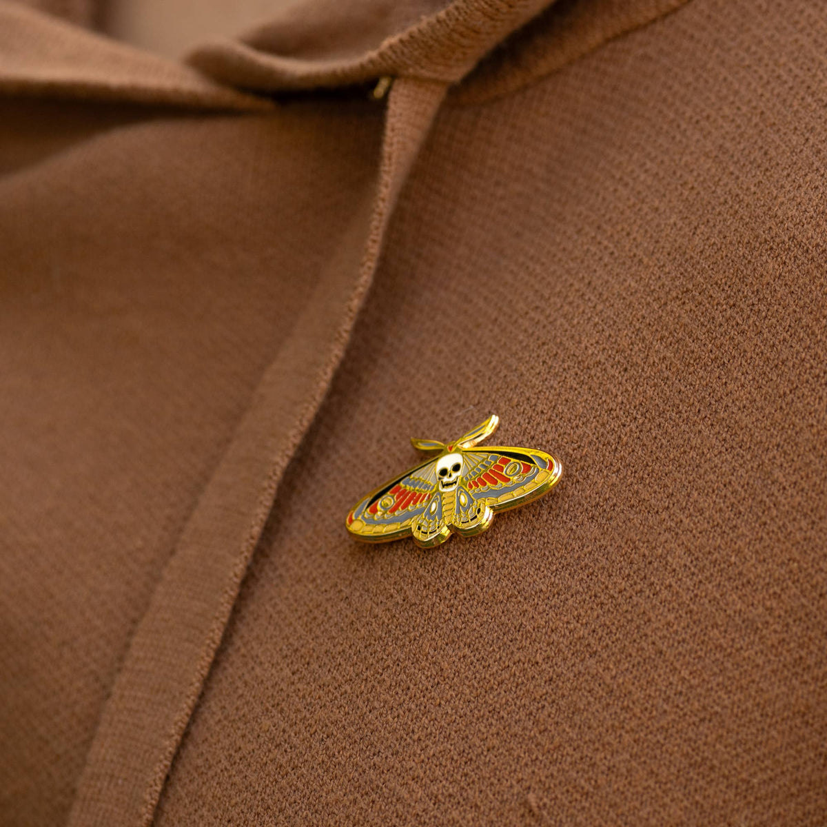 Gold enamel death moth skull pin on brown fabric