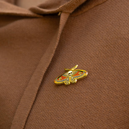Gold enamel death moth skull pin on brown fabric