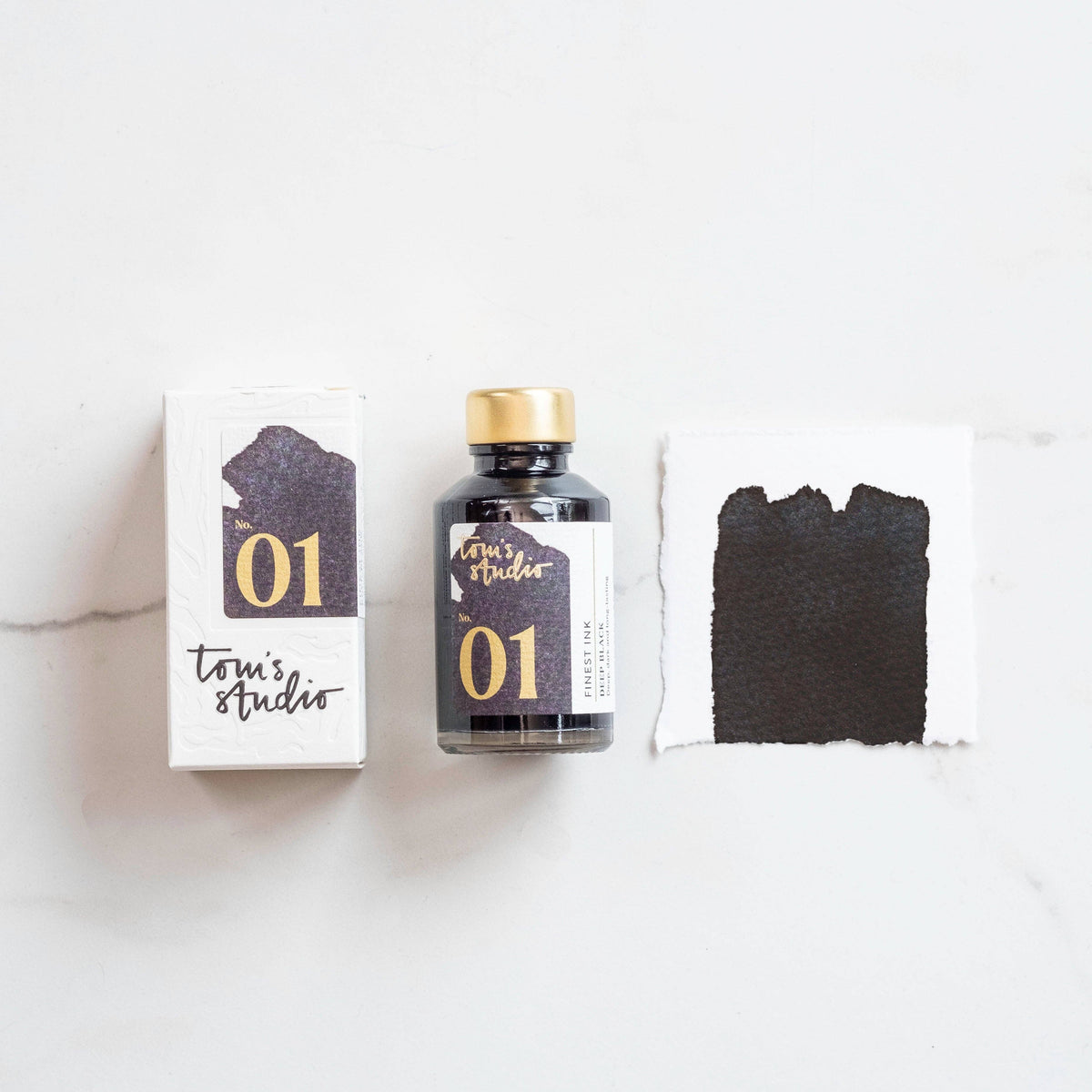 Deep black fountain pen ink bottle with gold cap, plus ink swatch and box labeled 01.
