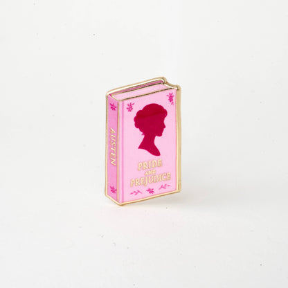 Pink book-shaped enamel pin with red silhouette and text 'Pride and Prejudice'.