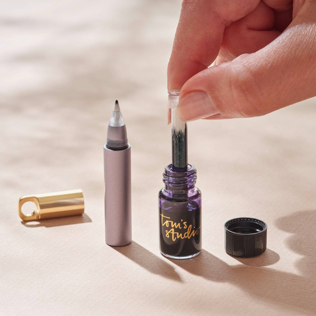 Refillable travel pen with gray barrel, gold cap, and inkwell refill beside it