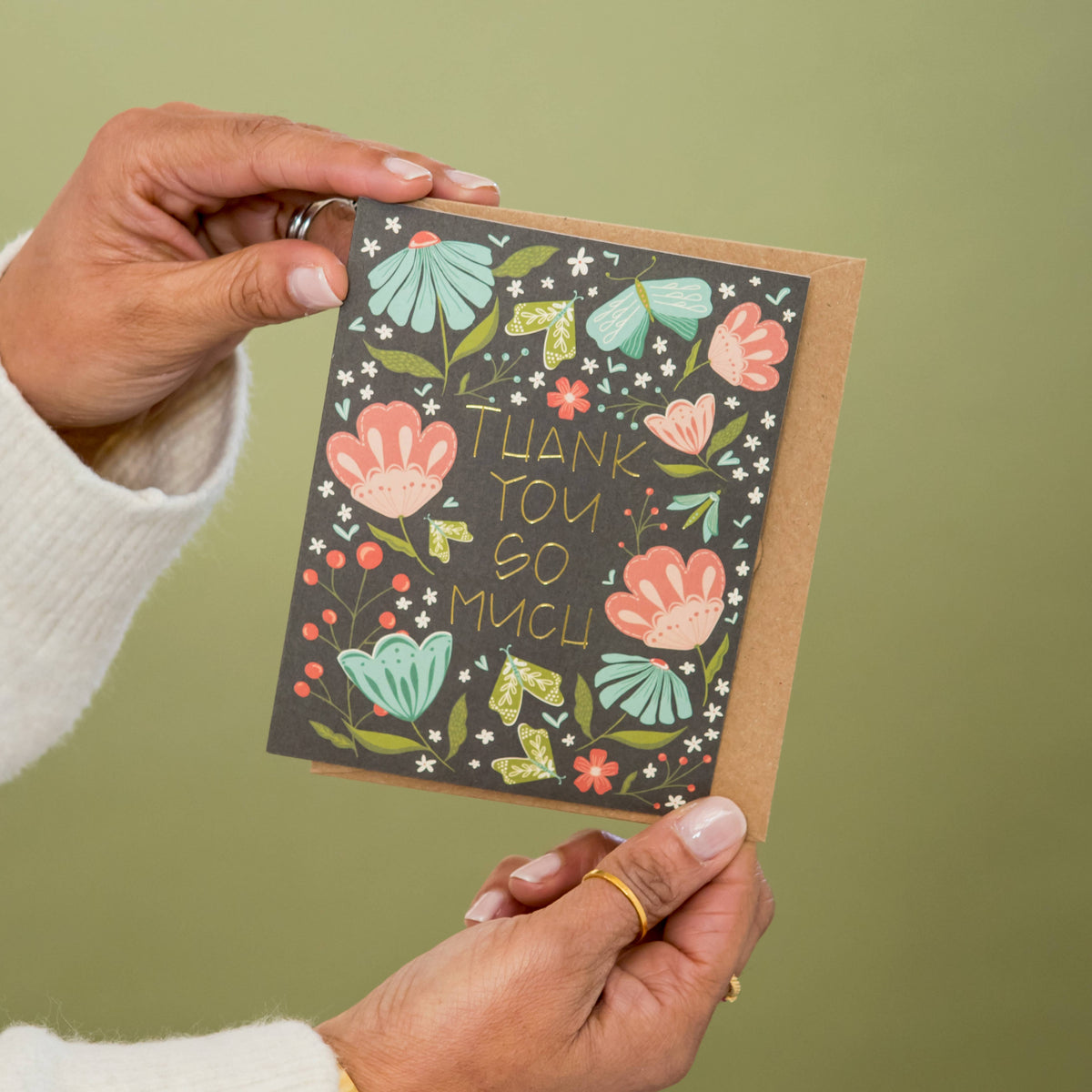 Floral thank-you greeting card with gold foil lettering, held open to show the design