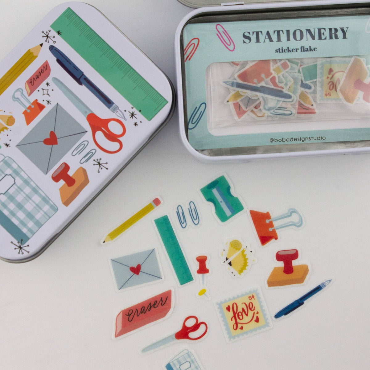 Stationery trinket tins with illustrated fronts and loose sticker flakes on a flat surface