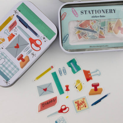 Stationery trinket tins with illustrated fronts and loose sticker flakes on a flat surface