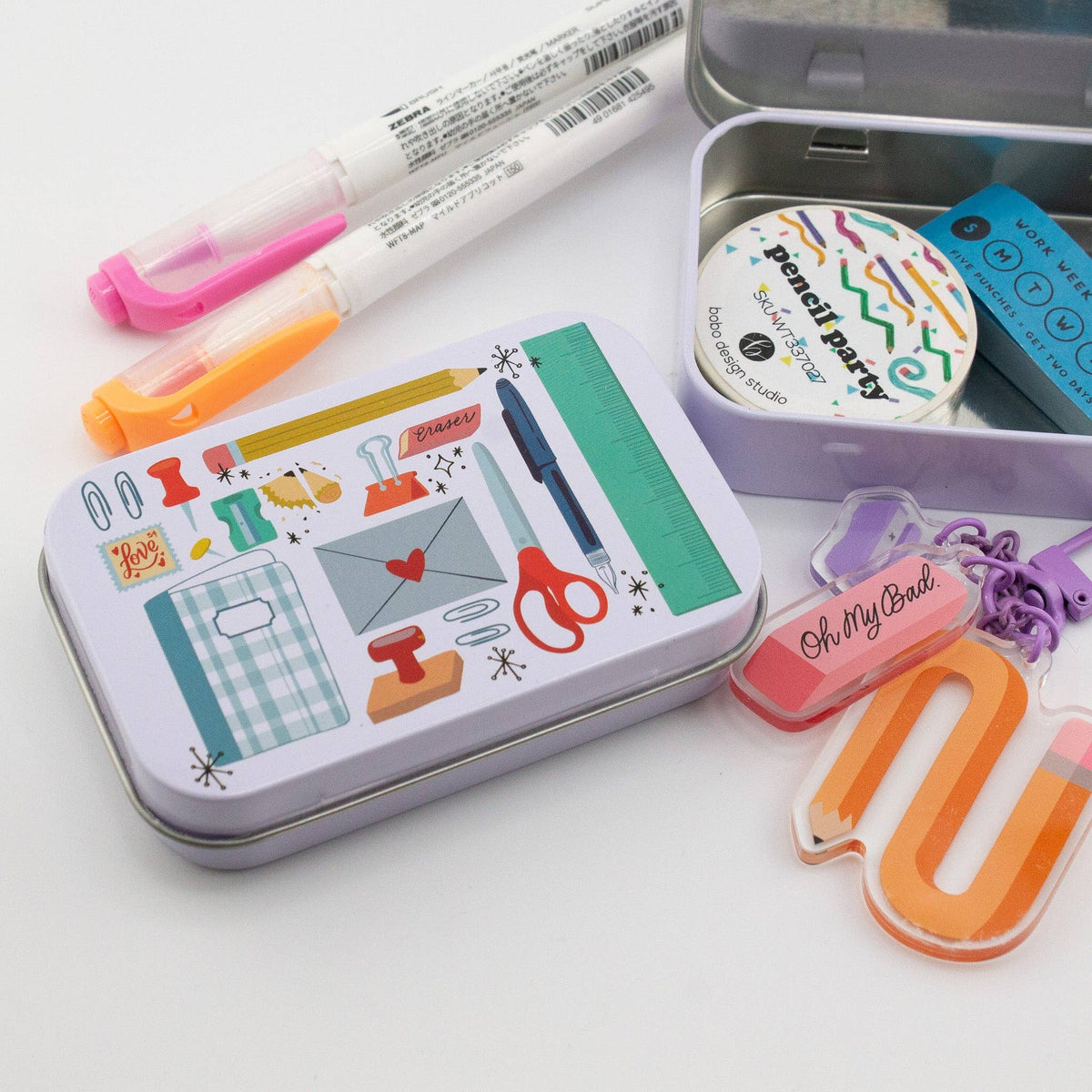 Stationery trinket tin with illustrated design, open tin, and colorful markers