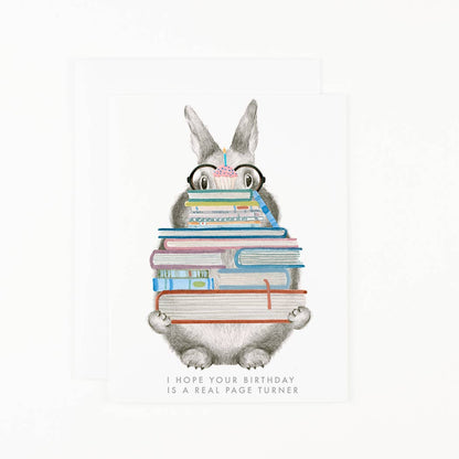Birthday card with grey rabbit holding stacked books and pink candle; message at bottom
