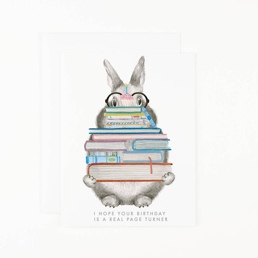 Birthday card with grey rabbit holding stacked books and pink candle; message at bottom