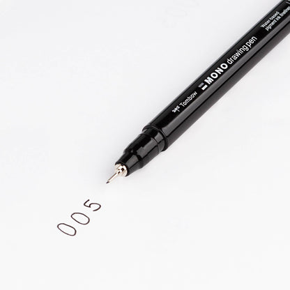 Black fine-tip drawing pen writing a small “0.5” sketch on white paper