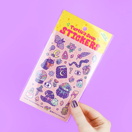 Pastel witch sticker sheet tilted in hand, featuring moon, star, crystal, potion icons