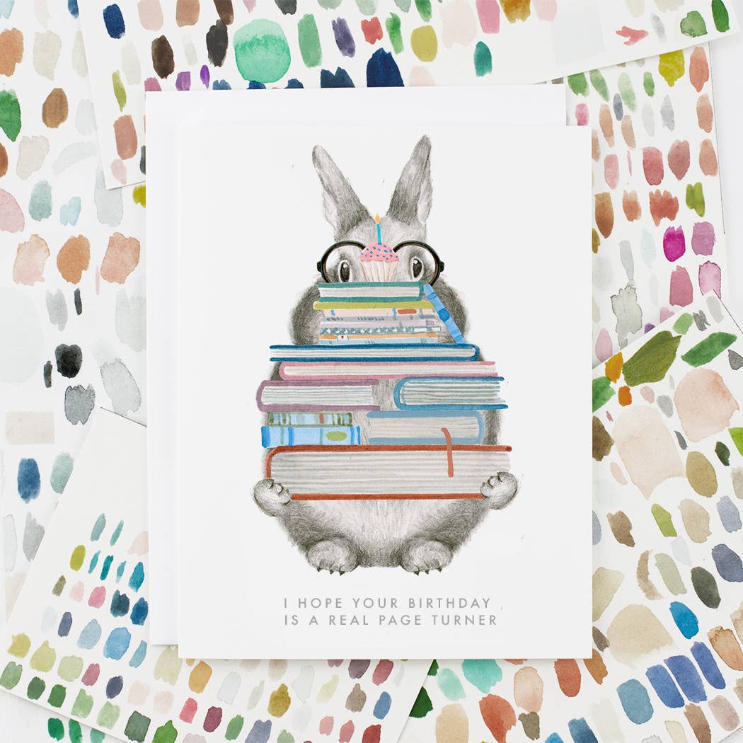 Birthday card with grey rabbit hugging stacked books and pink candle; “page turner” text