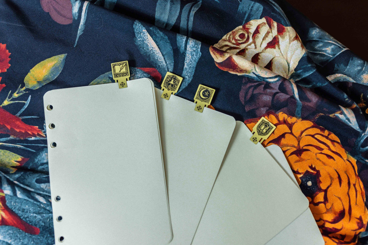 Three blank hole-punched pages with attached small gold square page markers