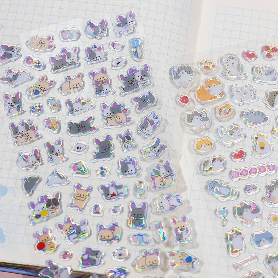 Close-up of clear holographic cat and character stickers on grid paper, assorted shapes.