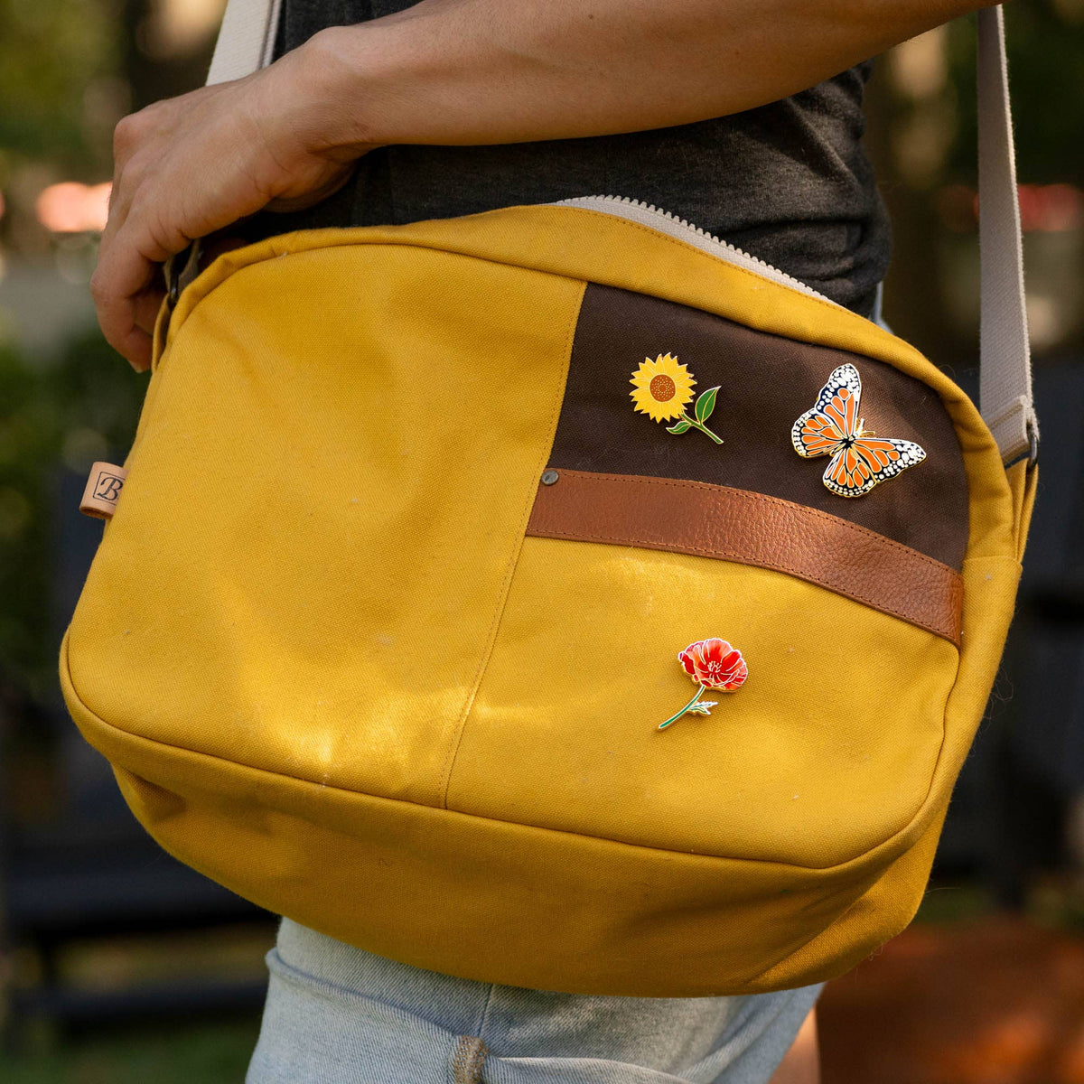 Monarch butterfly pin on a mustard crossbody bag flap.