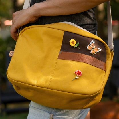 Monarch butterfly pin on a mustard crossbody bag flap.