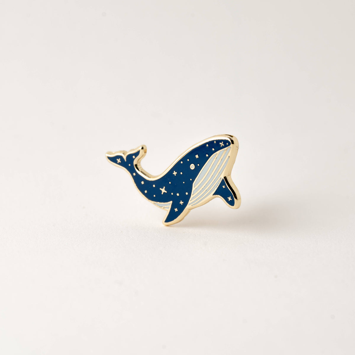 Small blue whale enamel lapel pin with gold outline and white belly