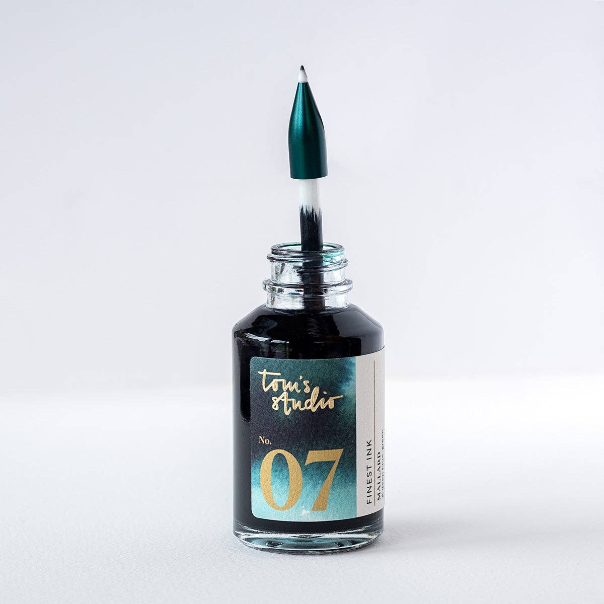 Glass ink bottle with green nib-tipped applicator on a dark base