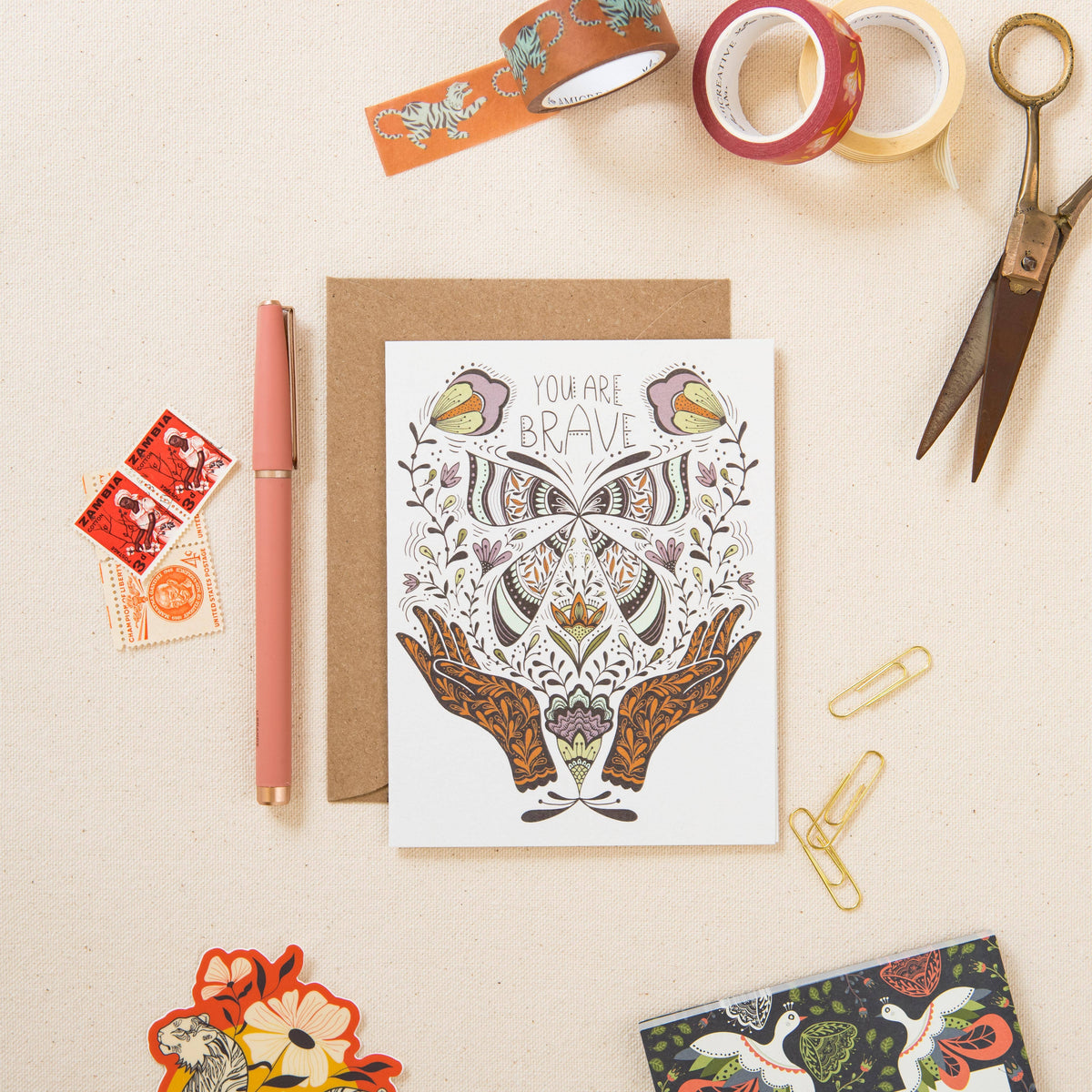 Greeting card with ornate butterfly and hands illustration, shown with kraft envelope.