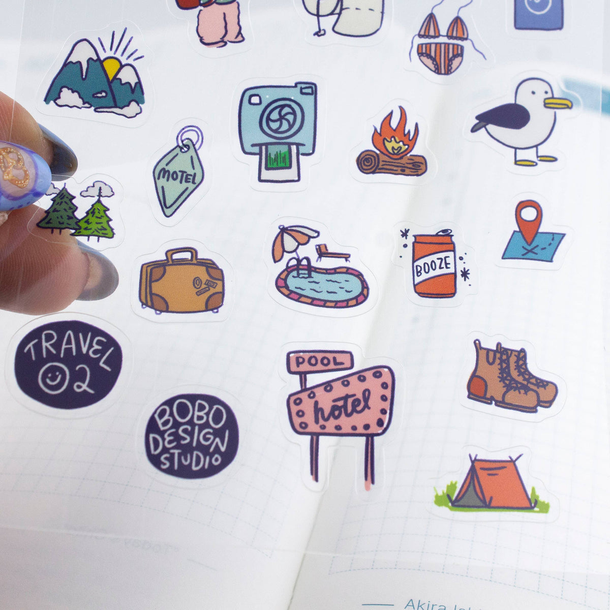 Detail view of clear sticker sheet with tent, luggage, pool sign, and boot stickers
