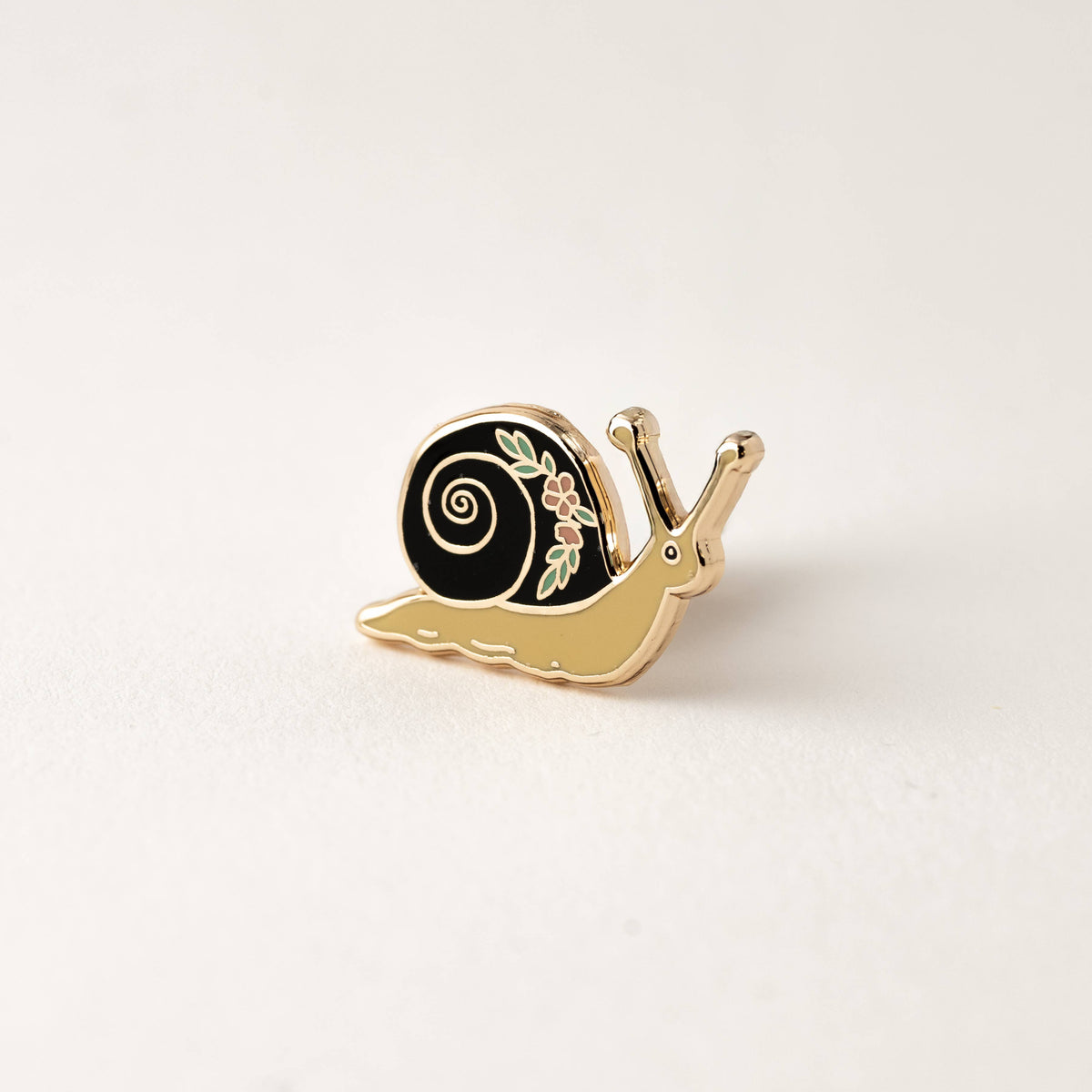 Enamel garden snail lapel pin with black swirl shell, gold-tone body, flower detail