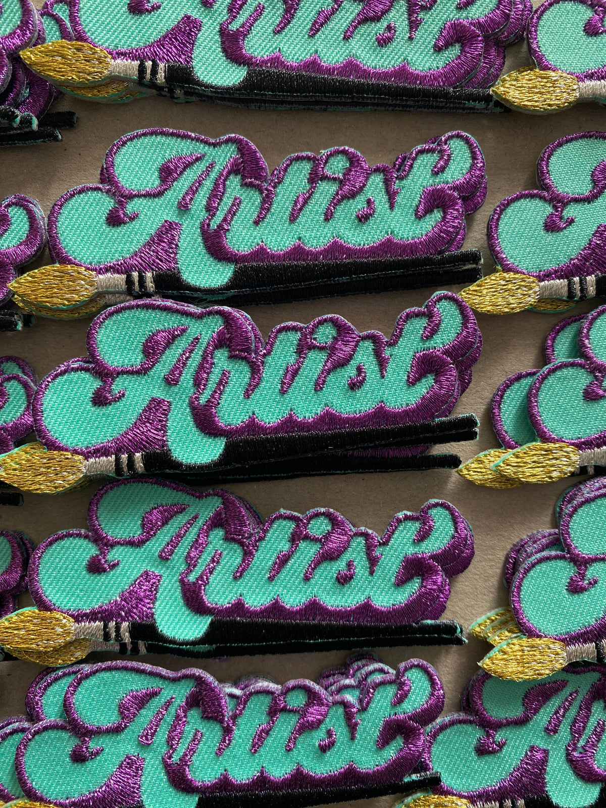 Iron-on patch detail: turquoise cursive lettering with purple stitching on black, yellow star tip