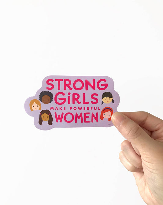 Hand holding a purple vinyl sticker reading “STRONG GIRLS” and “MAKE POWERFUL WOMEN”