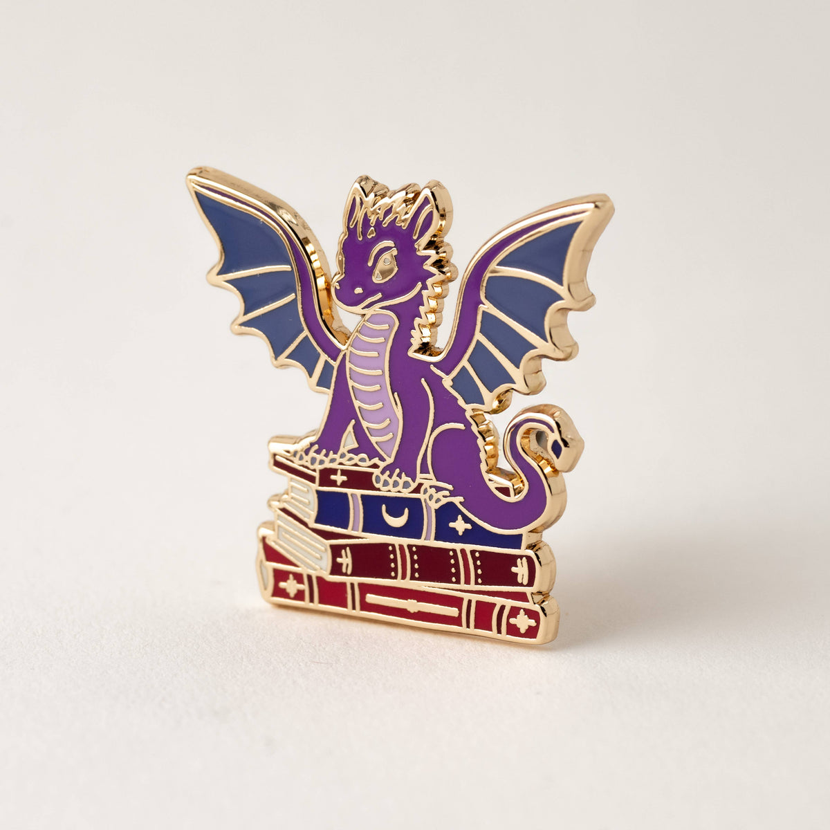 Purple dragon book enamel pin with wings and stacked books, gold accents