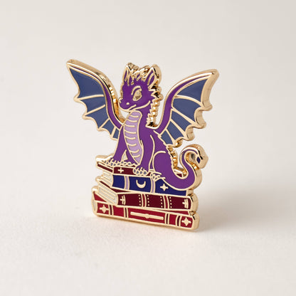 Purple dragon book enamel pin with wings and stacked books, gold accents