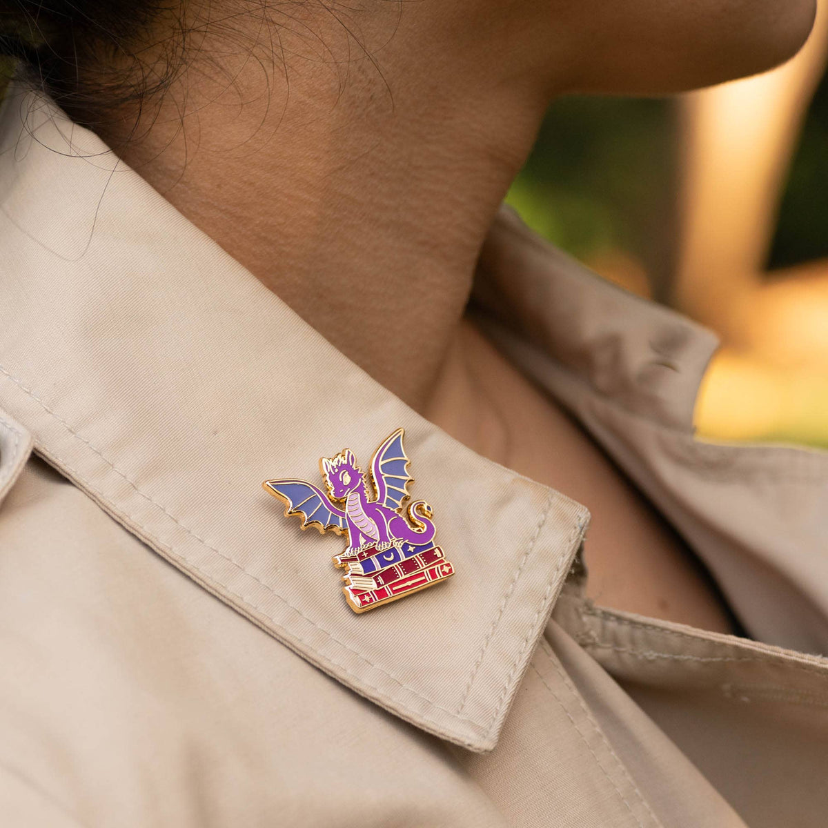 Dragon book pin on beige shirt collar, purple winged dragon over stacked books