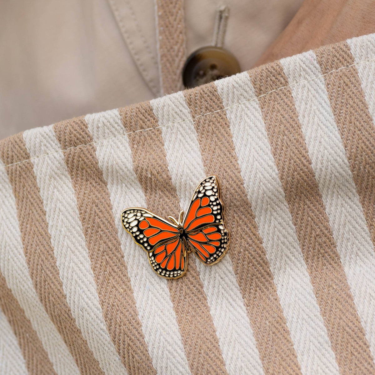 Monarch butterfly pin on a beige striped fabric surface.