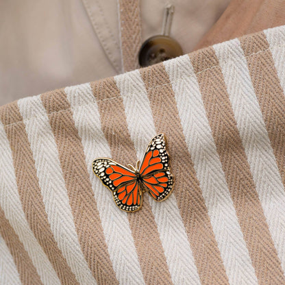 Monarch butterfly pin on a beige striped fabric surface.